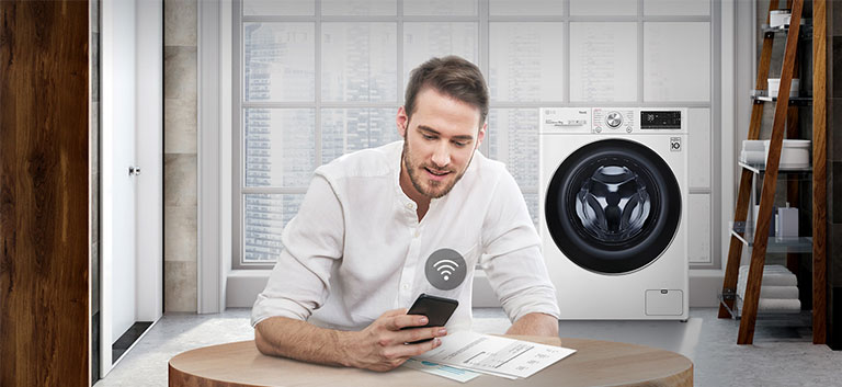 A man is monitoring the condition of the washing machine through a mobile phone app.