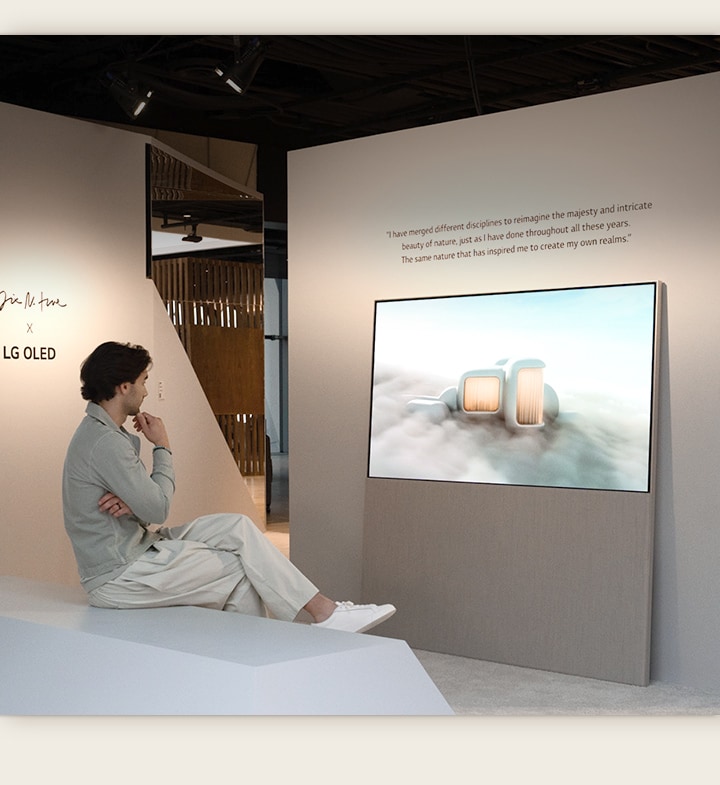 The image shows a person sitting on a chair looking at dreamlike scenery set among the clouds playing on Easel. On another wall, an LG OLED display shows an image of snow-covered trees reaching into the sky.