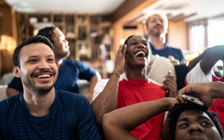 A group of men joyfully watching a football game on a calibrated TV, engrossed in laughter and smiles.