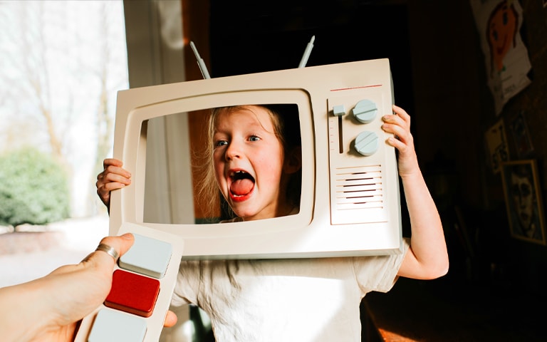 Child holding up a TV cut out with adult holding a toy tv remote, representing the process of calibrating a TV